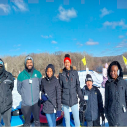 Five members of the Greer Center standing in a line in front of a tubing hill at Hawk Island on a sunny winter day.