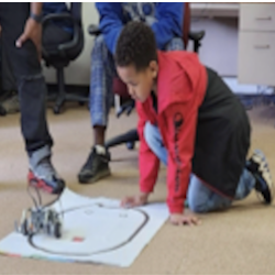 Photo of a child testing a robot they have programmed to follow an oval shape drawn on a paper